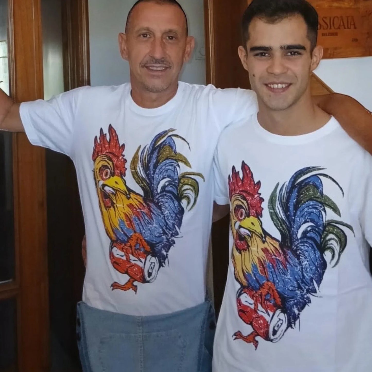 Due uomini sorridenti indossano magliette bianche ql maglie con gallo colorato e lattina stampati.