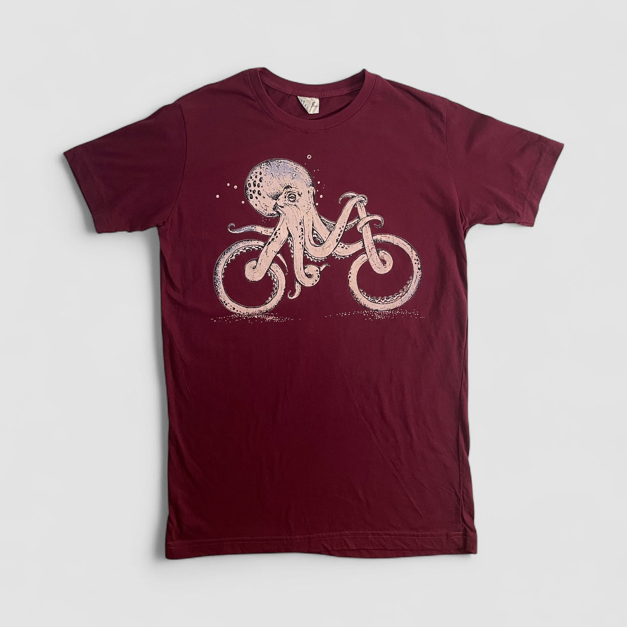 Maglietta bordeaux unisex in cotone con stampa artistica di un polpo che pedala una bicicletta, stile creativo e alternativo.