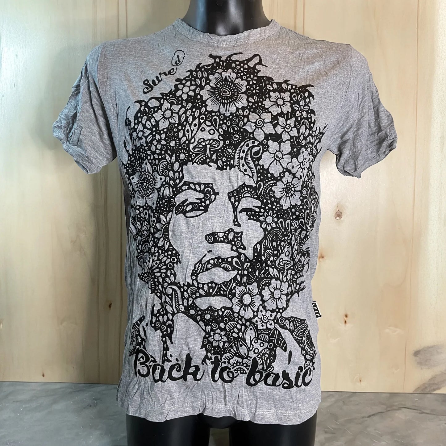 T-shirt grigia floreale con stampa artistica, frase 'Back to basic', esposta su manichino.