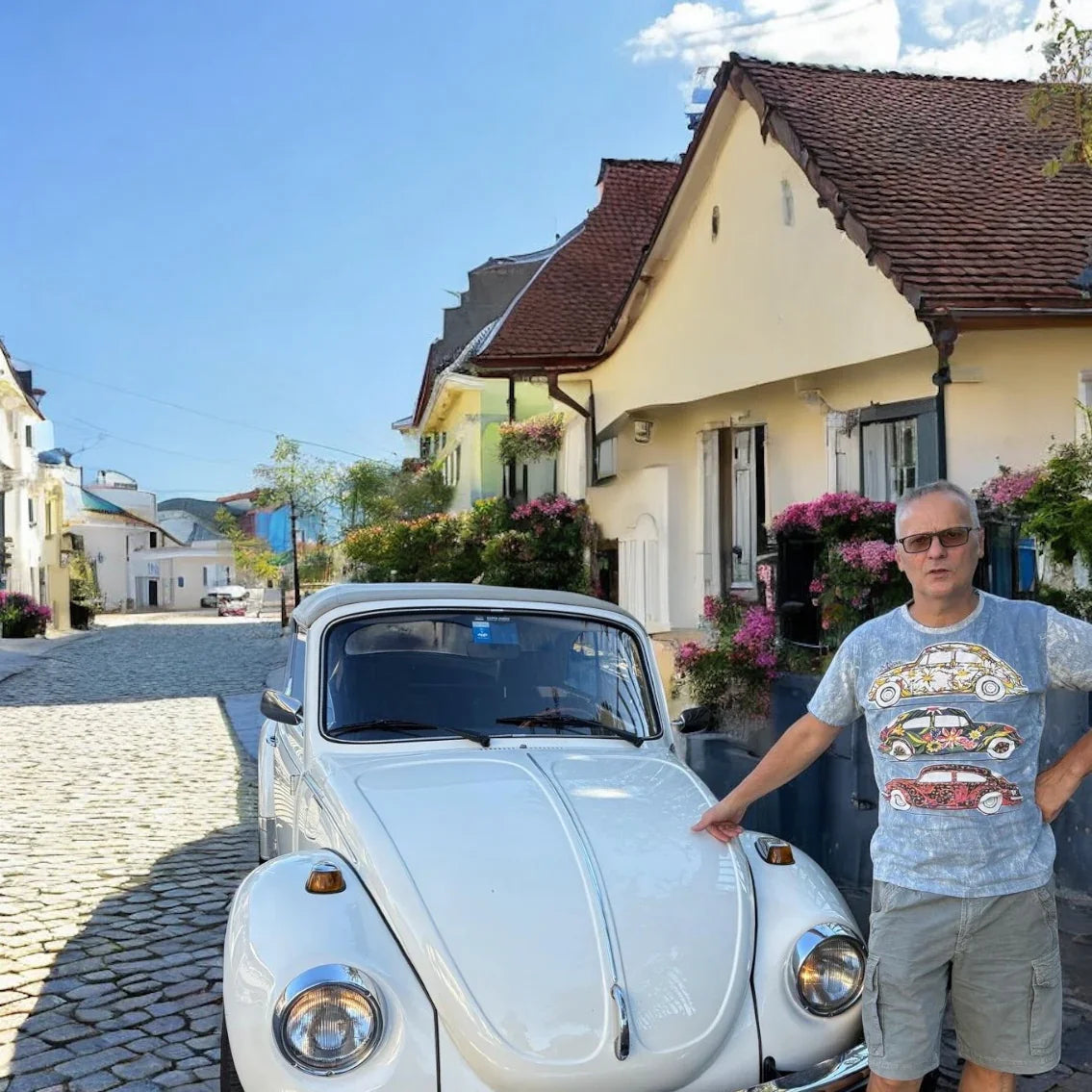 Uomo con maglietta maggiolini floreali vintage accanto a Volkswagen Beetle bianca in strada