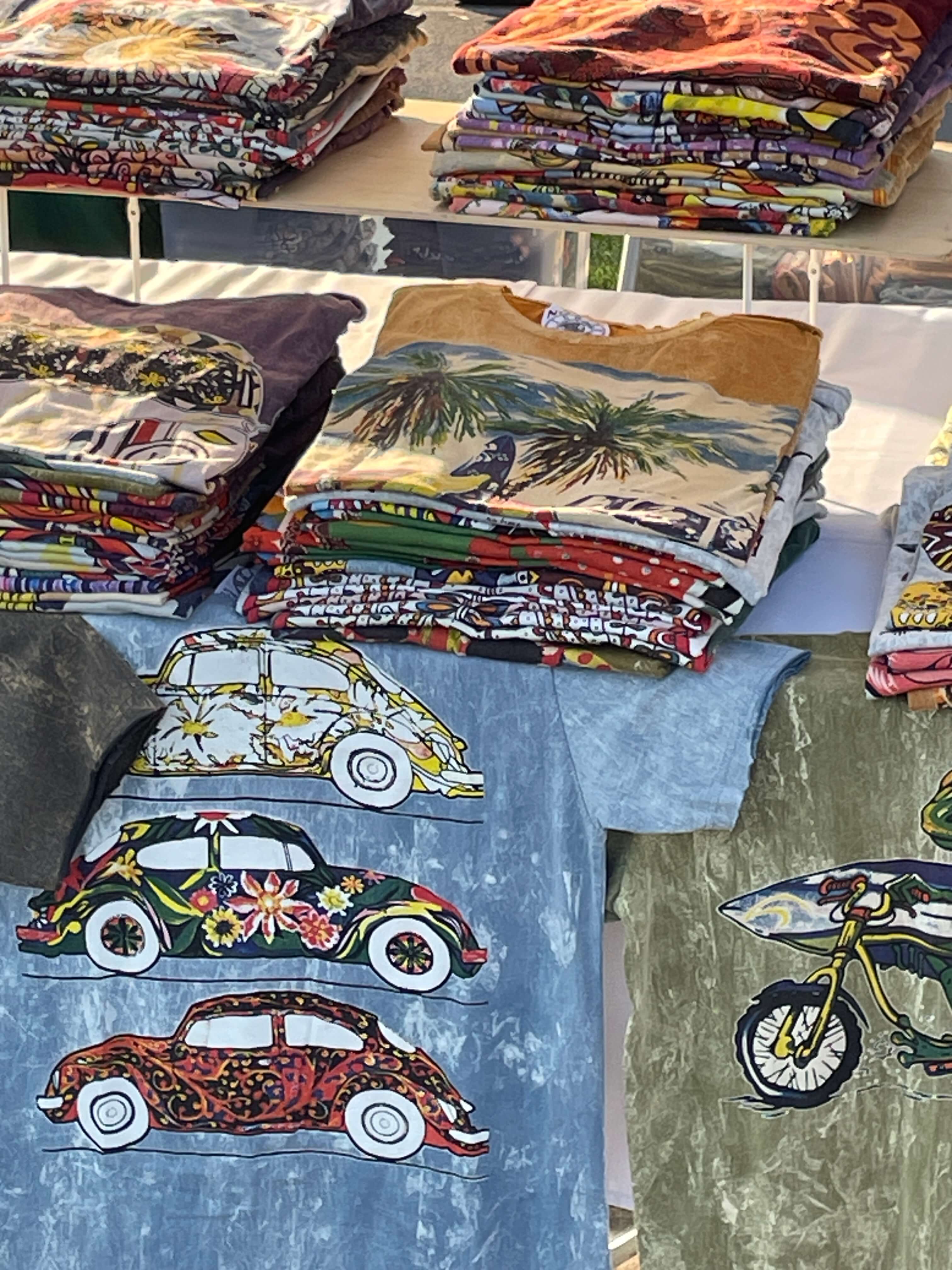 Esposizione di t-shirt artistiche QL Maglie con grafiche colorate ispirate a viaggi, surf, moto vintage e stile boho streetwear.