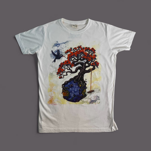 Maglietta bianca unisex in cotone con stampa artistica di un albero fiorito radicato in un pianeta blu e un uccello in volo.