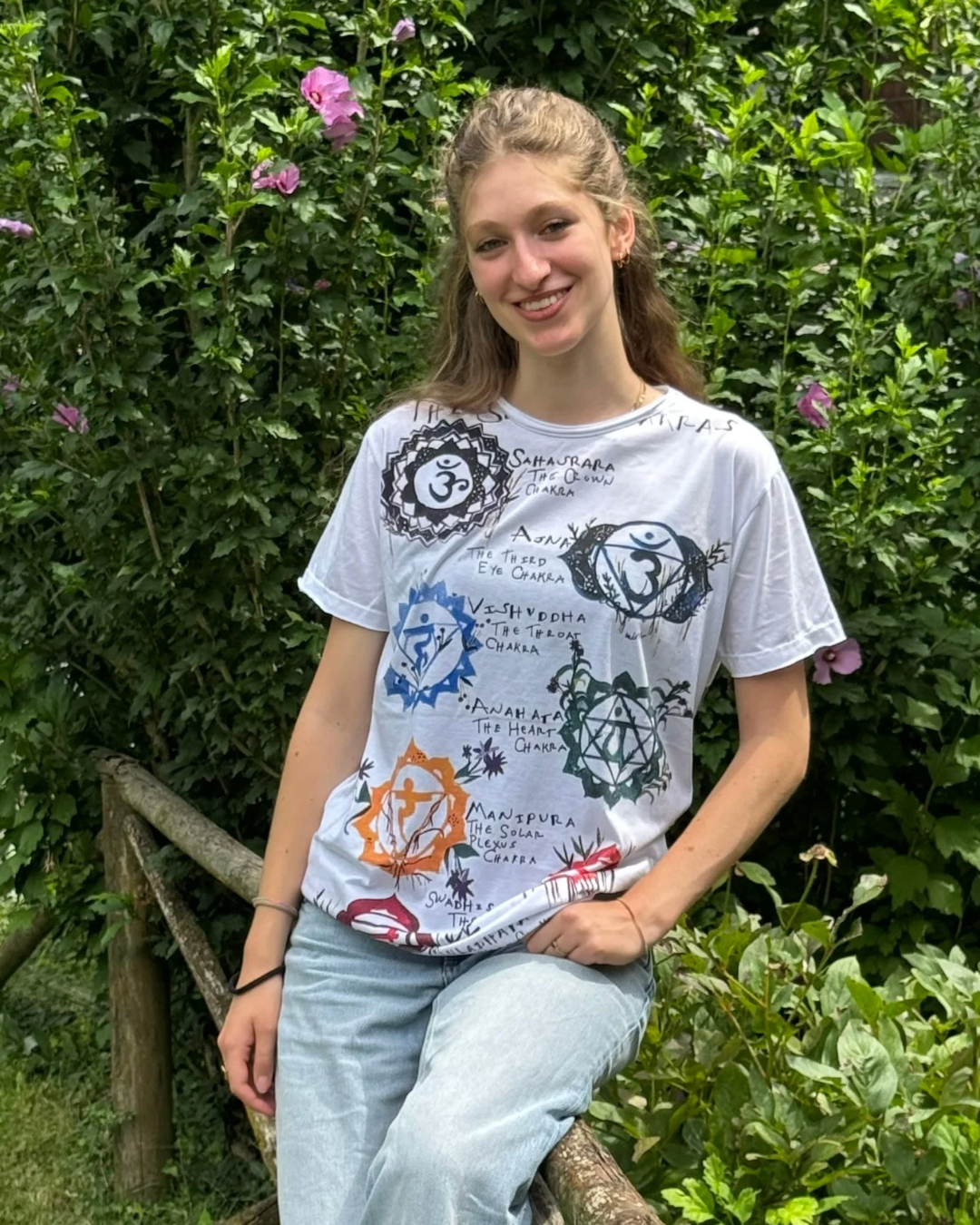 T-shirt bianca con illustrazione dei sette chakra e simboli energetici colorati, stile artistico, indossata.