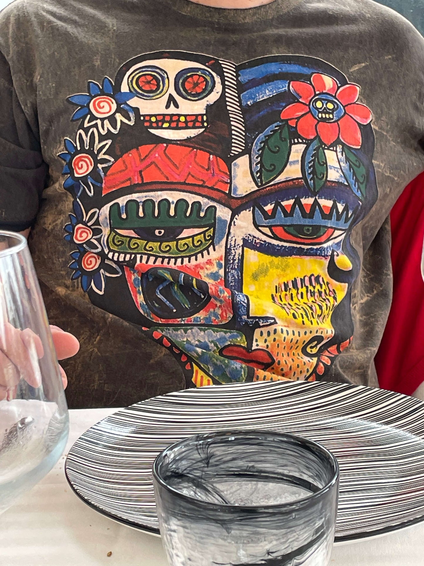 T-shirt unisex vintage con grande grafica multicolor raffigurante un volto astratto in stile tribale-folk, indossata, dettaglio ravvicinato.