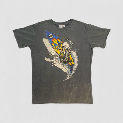 T-shirt vintage uomo con grafica di uno scheletro che surfa su una tavola con fiamme, sfondo effetto stone washed.