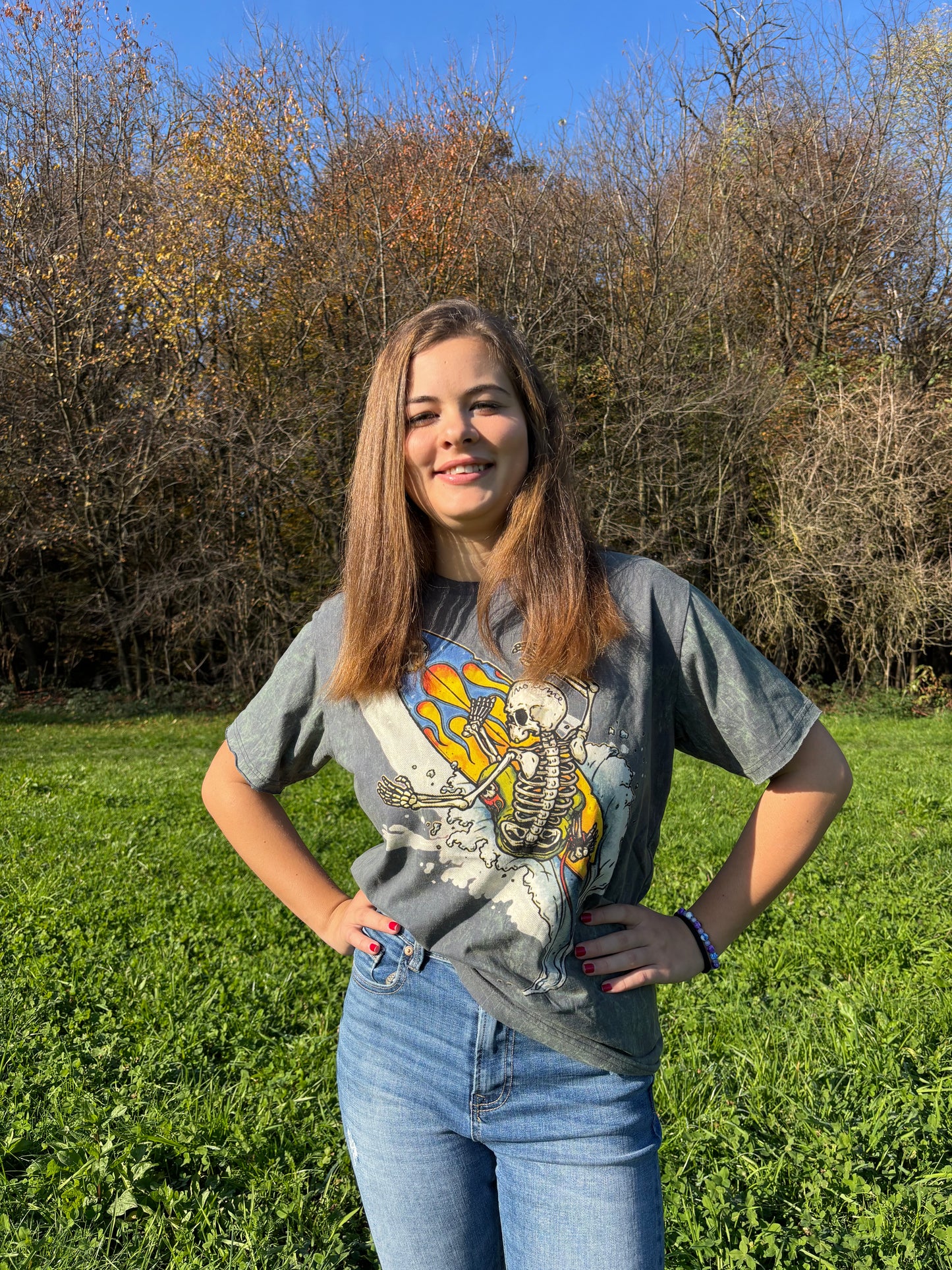 T-shirt vintage con grafica di uno scheletro che surfa su una tavola con fiamme, sfondo effetto stone washed.