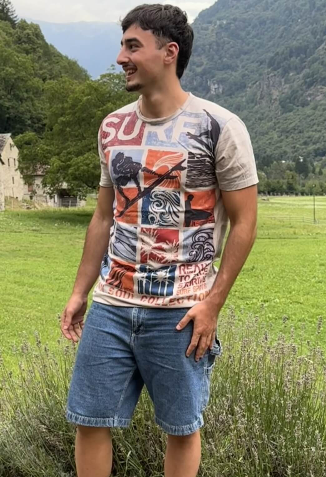 T-shirt stile surf vintage con grafica patch multicolore estate, indossata all’aperto in paesaggio naturale