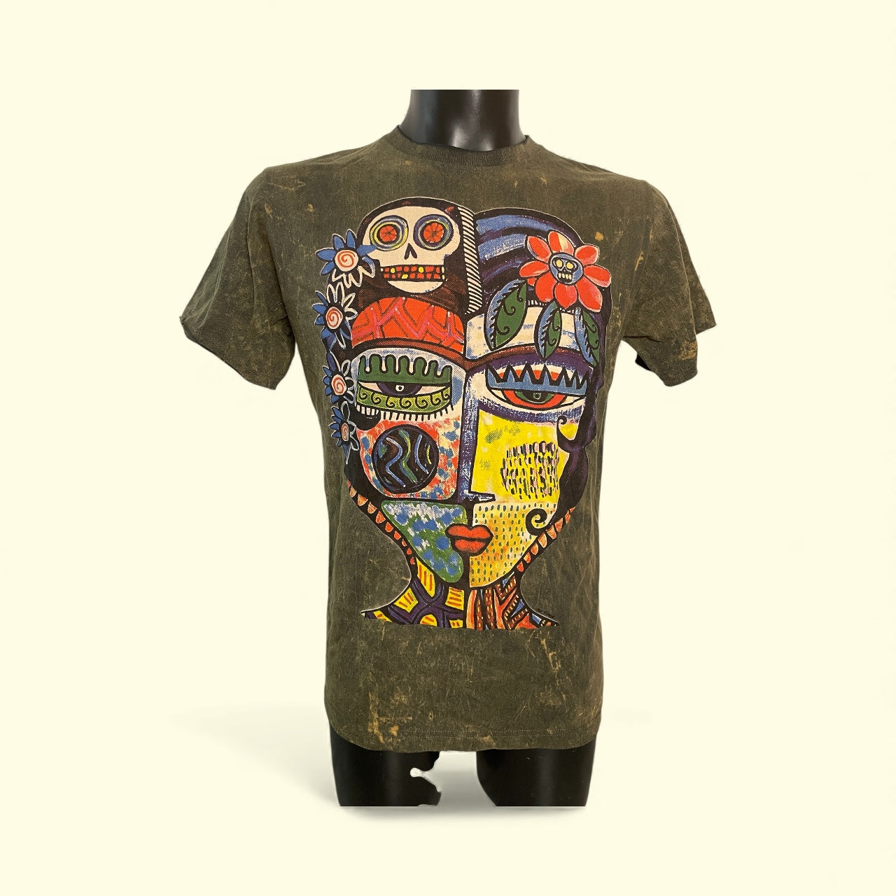 T-shirt unisex vintage con grande grafica multicolor raffigurante un volto astratto in stile tribale-folk su sfondo scuro, esposta su un manichino.